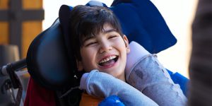 An elementary aged boy with dark hair smiling while sitting in a wheelchair